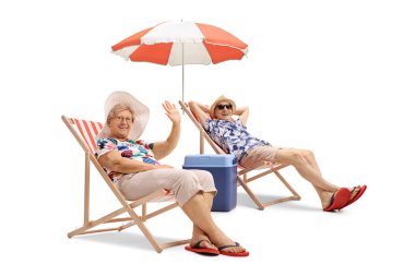 Yaşlı bir çift tatilde şemsiye altında şezlonglarda oturuyor ve beyaz arka planda izole bir şekilde el sallıyorlar.