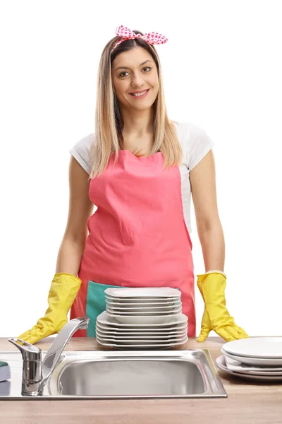 若い主婦白い背景に隔離されたきれいな料理とシンクの後ろにエプロンを身に着けています — ストック写真