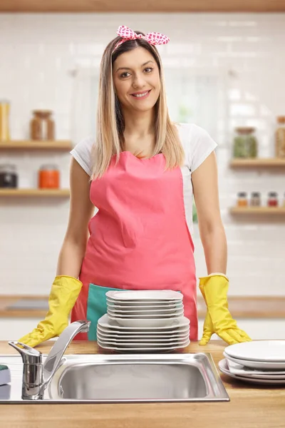台所できれいな料理とシンクの後ろにエプロンを身に着けている若い女性 — ストック写真