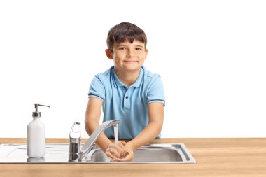 Çocuk lavaboda ellerini yıkıyor ve beyaz arka planda izole edilmiş kameraya bakıyor.