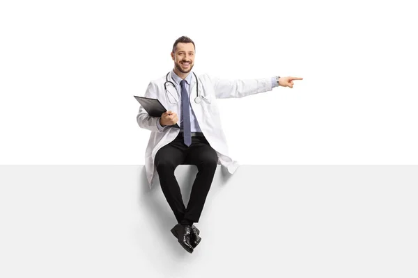 Male Doctor Sitting Blank Panel Pointing Side Isolated White Background — Stock Photo, Image