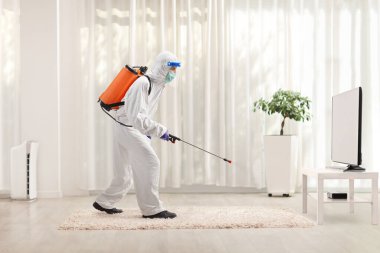 Man in a hazmat suit sanitising a room in an apartmemt clipart