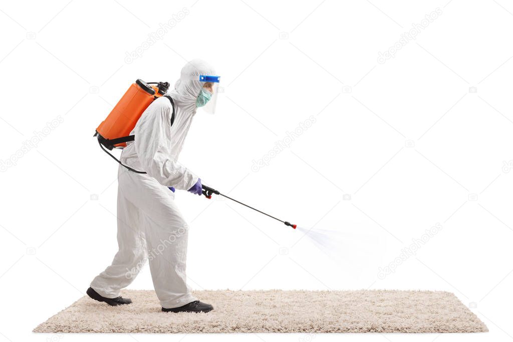 Full length profile shot of a man in a hazmat suit spraying a disinfectant on a carpet isolated on white background