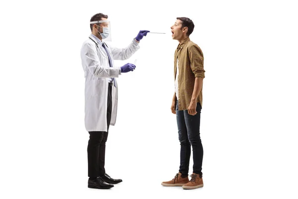 白い背景に隔離された若い男から綿棒のテストを受けて顔の盾を持つ医師の完全な長さプロファイルショット — ストック写真