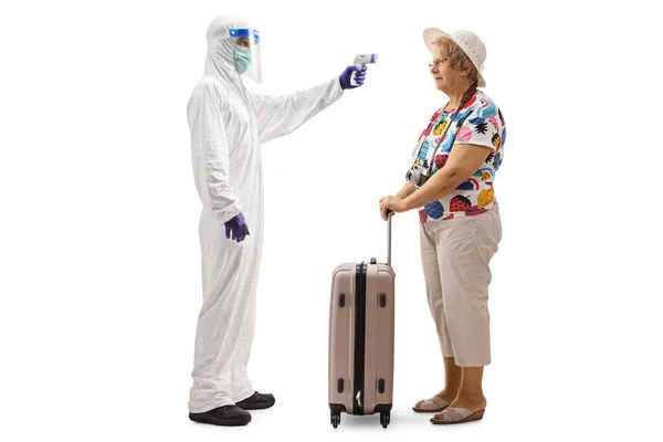 白い背景に隔離されたスーツケースを持つ高齢女性観光客への温度を測定するハズマットスーツの男の完全な長さプロファイルショット — ストック写真