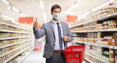 Süpermarkette sepet alışverişi yapan, resmi kıyafetli ve koruyucu maske takan bir adam. 