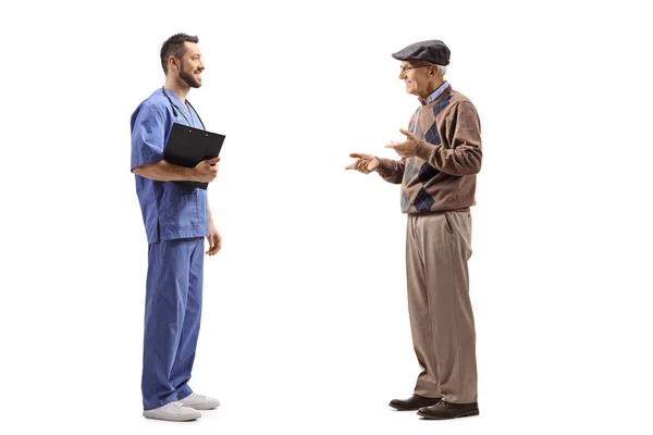 白い背景に隔離された高齢者と話をする青い制服を着た男性医師の完全長プロファイルショット — ストック写真