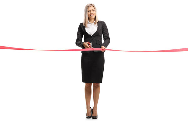 Full length portrait of a businesswoman cutting a red tape on a formal event isolated on white background