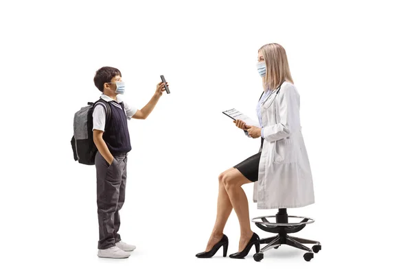 一名身穿制服 戴口罩的男中学生的全长侧面照片 照片上的女医生带着智能手机 与白人背景隔离 — 图库照片