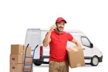 Teslimatçı cep telefonuyla konuşuyor ve beyaz arka planda izole edilmiş bir minibüsün önünde bir paket tutuyor.