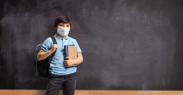 学校の黒板の前にはリュックや本が置かれ 保護面のマスクをしている少年 — ストック写真