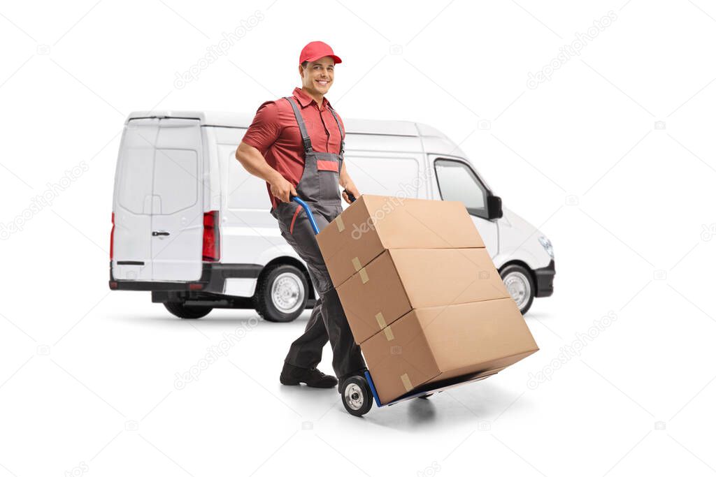 Male worker in a uniform pushing a hand truck loaded with boxes in front of a white van isolated on white background