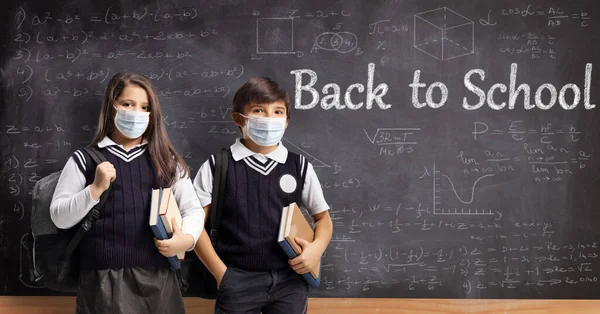 女子校生と女子校生保護マスクを学校の黒板の前に立ちテキストを学校に戻す — ストック写真