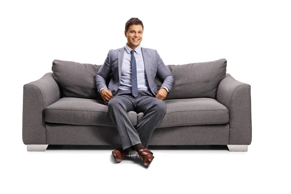 穿着雅致衣服的男人坐在沙发上 面带微笑地孤零零地坐在白色的背景上 — 图库照片
