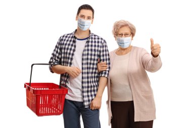Boş bir alışveriş sepeti olan genç bir adam ve beyaz arka planda maskeli yaşlı bir kadın. 