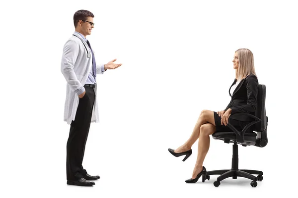 白い背景に隔離された椅子に座っている実業家と話して立っている男性医師の完全な長さのプロフィールショット — ストック写真