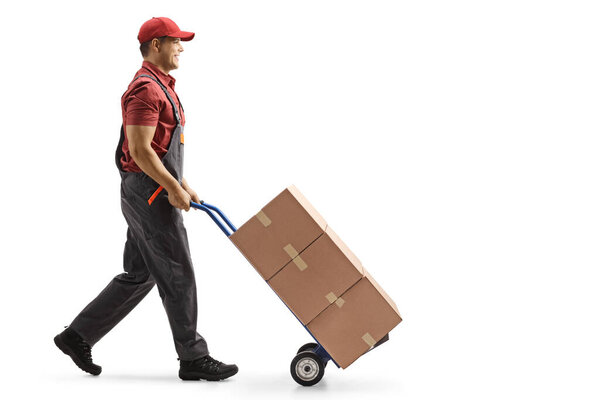 Full length profile shot of a male worker pushing boxes on a hand-truck isolated on white background