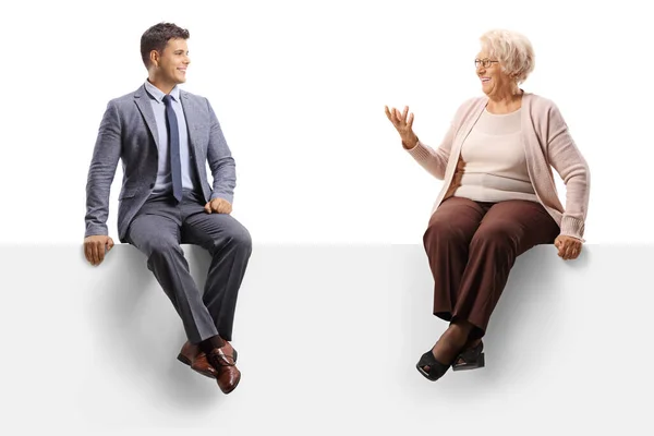 上了年纪的女人坐在一块空白的板子上 与一个有着白色背景的英俊的年轻人交谈 — 图库照片