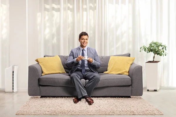 プロの若い男が自宅でソファに座ってコーヒーを飲みながら — ストック写真