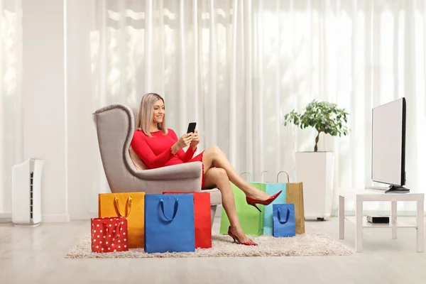 家の床に携帯電話とショッピングバッグを持つアームチェアに座っている女性 — ストック写真