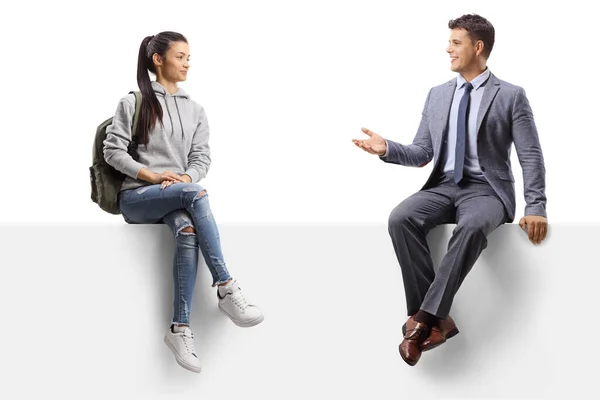 Female student sitting on a blank panel and talking to a man in a suit isolated on white background