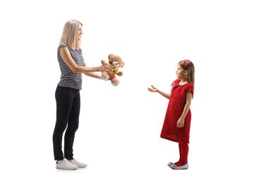 Bir annenin beyaz arka planda izole edilmiş kızına oyuncak ayı verirken tam boy profil fotoğrafı.