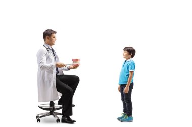 Erkek dişçi, beyaz arkaplanda izole edilmiş bir çocuğa model bir çene ile fırçalamayı gösteriyor.