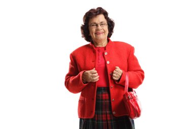 Yaşlı bir kadın gülümsüyor ve beyaz arka planda kırmızı bir el çantası tutuyor.