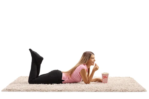 年轻女人躺在地毯上 吃着被白色背景隔开的爆米花 — 图库照片