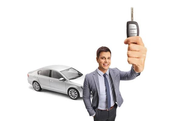 一个专业的年轻人在一辆白色背景的银色轿车前展示了一把汽车钥匙 — 图库照片