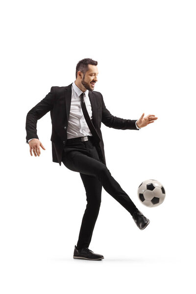 Full length shot of a man in suit and tie kicking a football isolated on white background