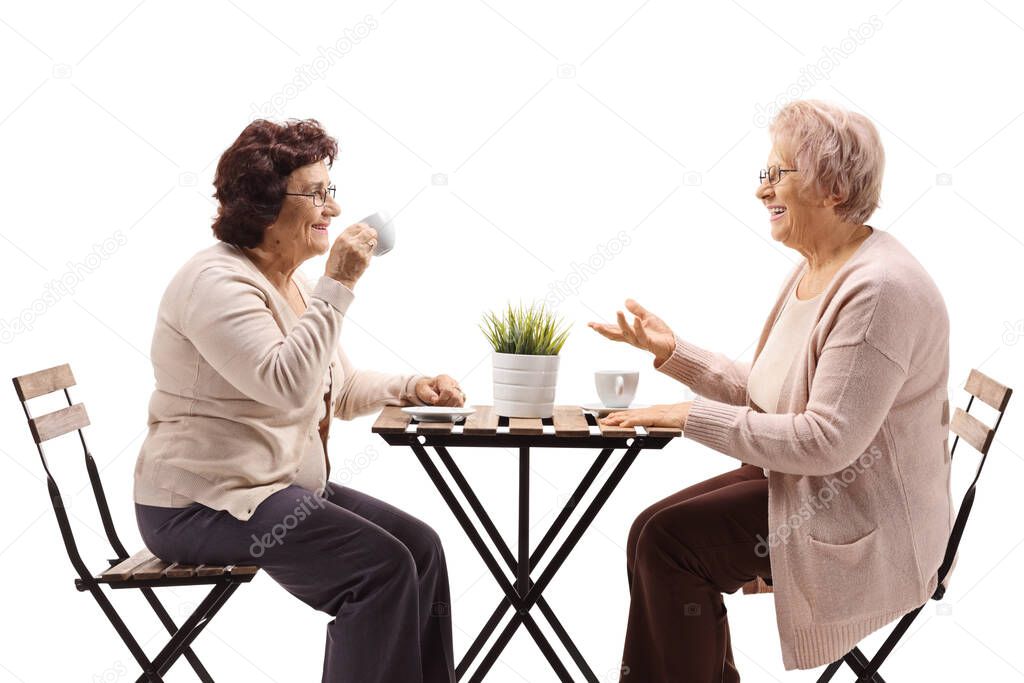 Elderly female friends drinking coffee at a table and talking isolated on white background