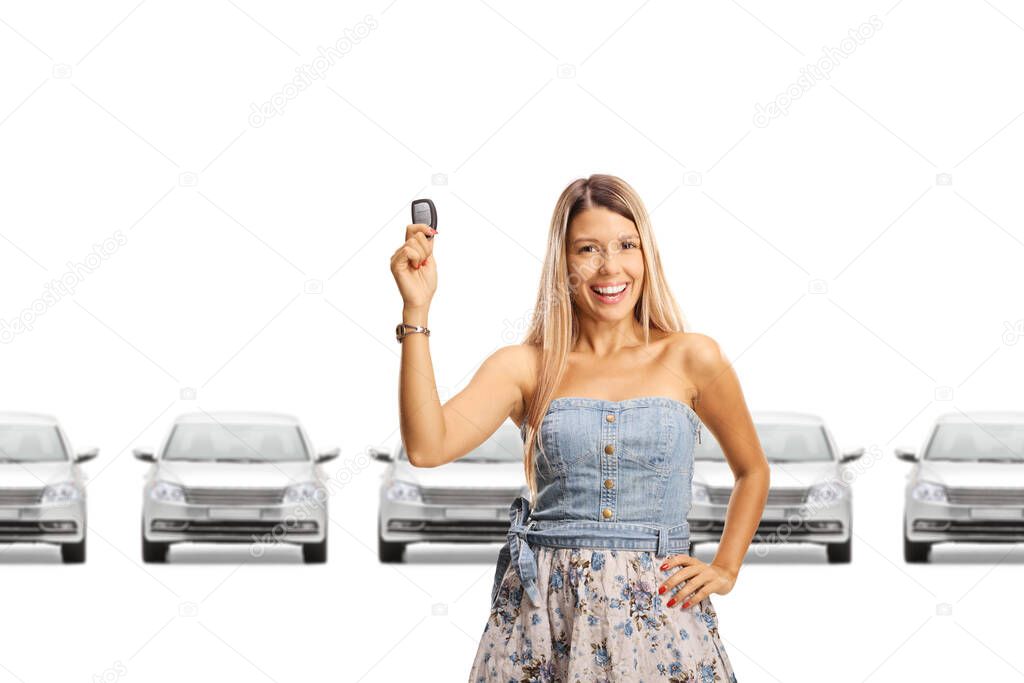 Happy young woman holding a car key and smiling in a showroom isolated on white background 