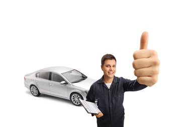 Arkasında gümüş bir araba olan otomobil tamircisi beyaz arka planda baş parmaklarını gösteriyor.