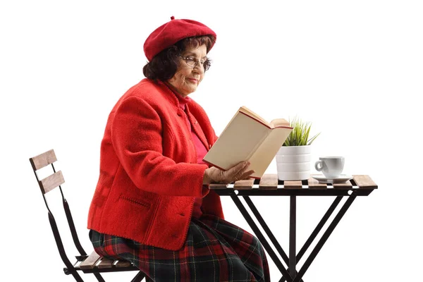 在咖啡馆桌旁的一个成熟女人正在阅读一本以白色背景为背景的书 — 图库照片