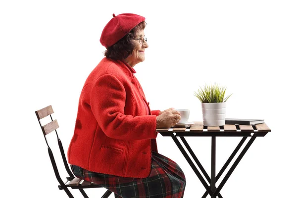 在白底隔离的桌子边喝咖啡的老年妇女 — 图库照片