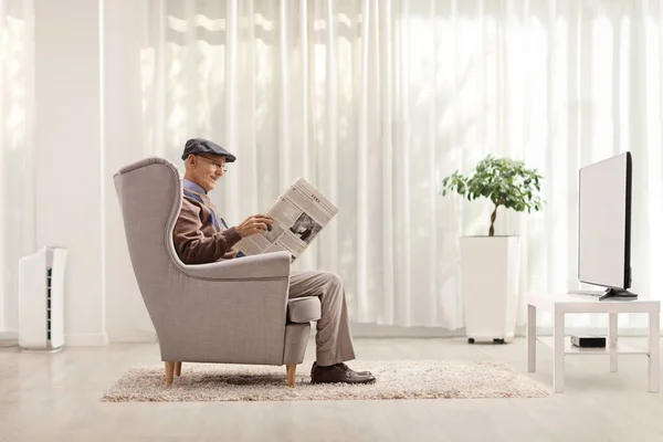 老人坐在扶手椅上 在家里的客厅里看报纸 — 图库照片