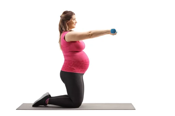 妊娠中の女性がマットの上でひざまずき 白い背景に隔離されたダンベルで運動するフル長プロファイルショット — ストック写真