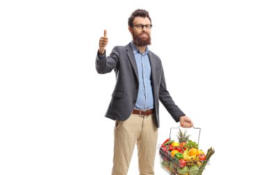 Sakallı adam elinde meyve ve sebzelerle dolu bir sepet beyaz arka planda parmaklarını gösteriyor.