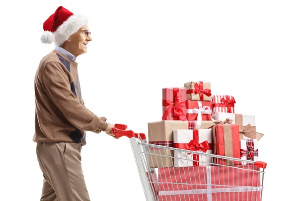 头戴圣诞礼帽 头戴圣诞礼帽的老人推着一辆白色背景的圣诞礼物购物车 — 图库照片