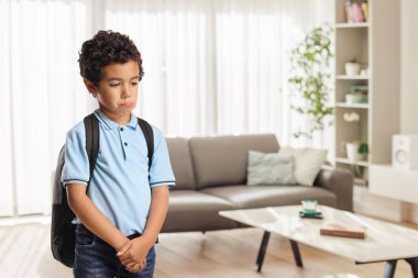 Evde tek başına duran sırt çantalı üzgün çocuk.