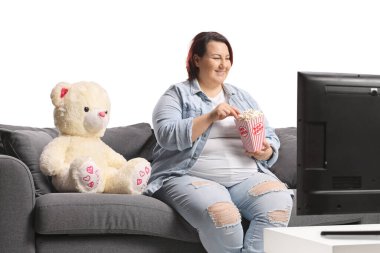 Kanepeye oturmuş televizyon seyreden ve beyaz arka planda izole edilmiş patlamış mısır yiyen bir kadın.