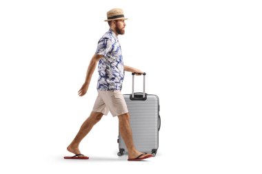 Beyaz arka planda izole edilmiş bir bavulu yürüten ve yuvarlayan bir adamın tam boy profil çekimi.