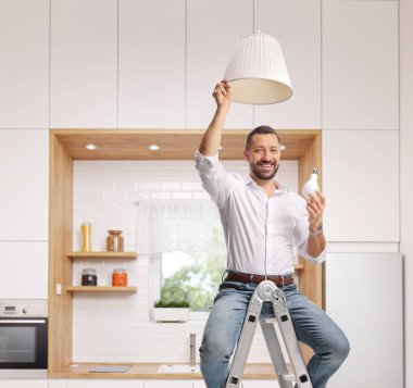 Kolye lambası için ampul tutan ve mutfaktaki merdivenin tepesinde oturan bir adam.