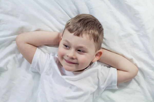 O bonitinho está deitado na cama. Um menino de 4 anos joga na cama. Criança feliz. Recreação. Dorme. Bom dia. Aconchegante . — Fotografia de Stock