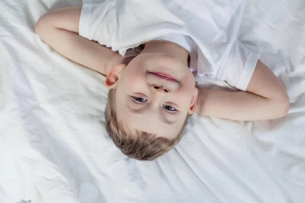 Χαριτωμένο μικρό αγόρι ξαπλωμένη στο κρεβάτι. Ένα αγόρι 4 ετών παίζει στο κρεβάτι. Ευτυχισμένο παιδί. Αναψυχής. Ύπνου. Το πρωί. Άνετο. — Φωτογραφία Αρχείου