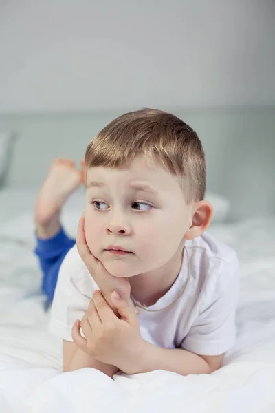 Söt liten pojke ligger på sängen. En 4-årig pojke spelar på sängen. Lyckligt barn. Rekreation. Sova. Morgon. Cozy. — Stockfoto