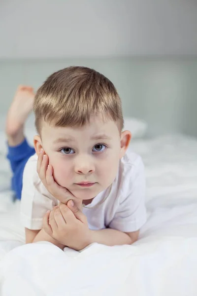 O bonitinho está deitado na cama. Um menino de 4 anos joga na cama. Criança feliz. Recreação. Dorme. Bom dia. Aconchegante . — Fotografia de Stock