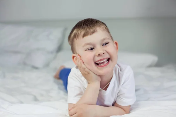 Schattige kleine jongen is liggend op het bed. Een 4-jarige jongen speelt op het bed. Gelukkig kind. Recreatie. Slaap. Ochtend. Gezellige. — Stockfoto