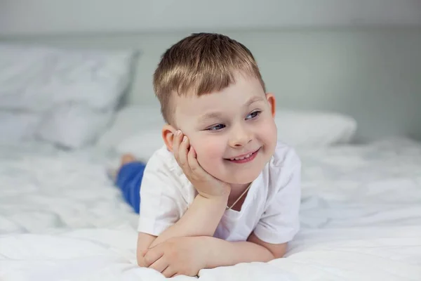 O bonitinho está deitado na cama. Um menino de 4 anos joga na cama. Criança feliz. Recreação. Dorme. Bom dia. Aconchegante . — Fotografia de Stock